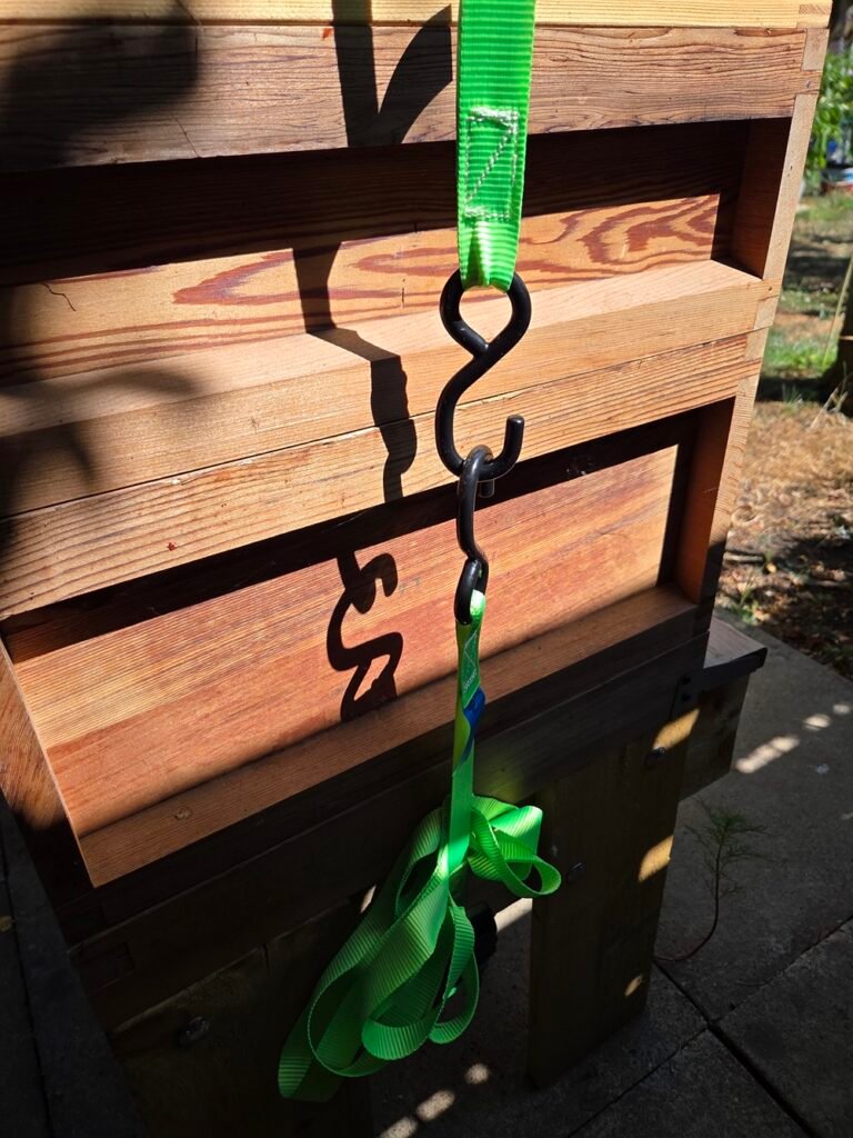 Close-up of a bright green hive strap secured with black S-hooks against the side of a cedar wood National beehive
