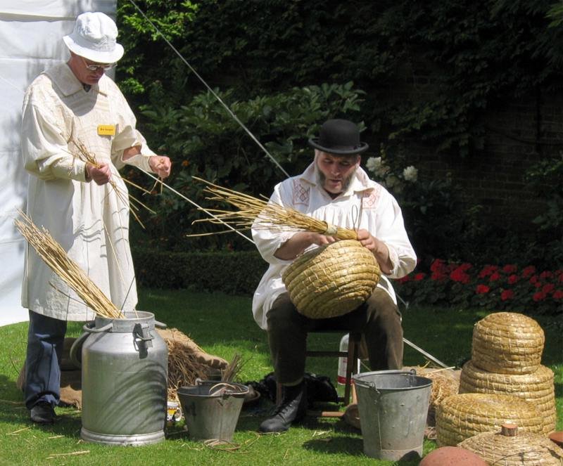 Craftsmen weaving traditional straw bee skeps using coiled lipwork basketry outdoors